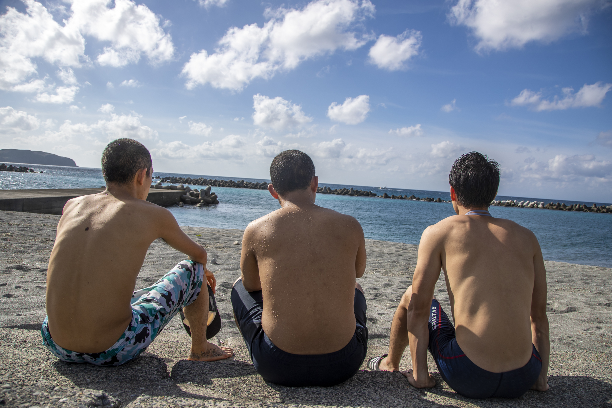 海パン姿で前浜海岸に腰掛ける3人の背中