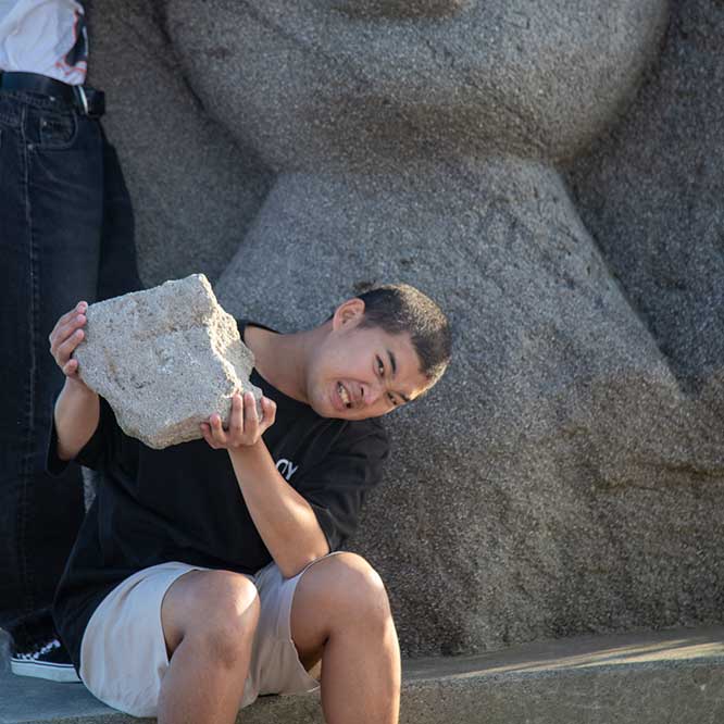 石像の前で大きな石を持ち上げる後藤さん