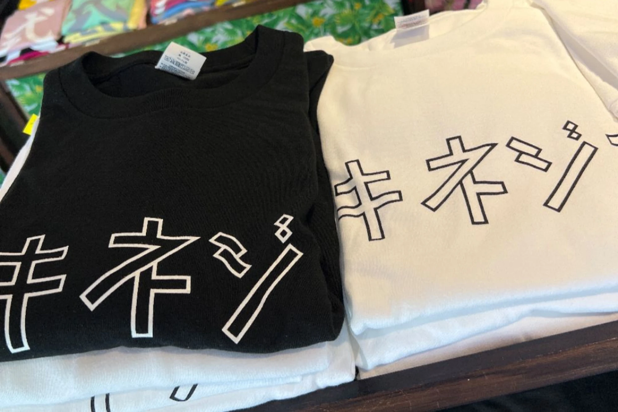「レンタサイクルまんぼう」で販売されている「シキネジマ」の大きなカタカナのロゴが入ったTシャツ。シンプルな白地に黒文字、黒地に白文字の2色展開