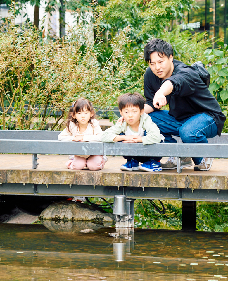 メインビジュアル：橋の上で屈んで池を眺める家族