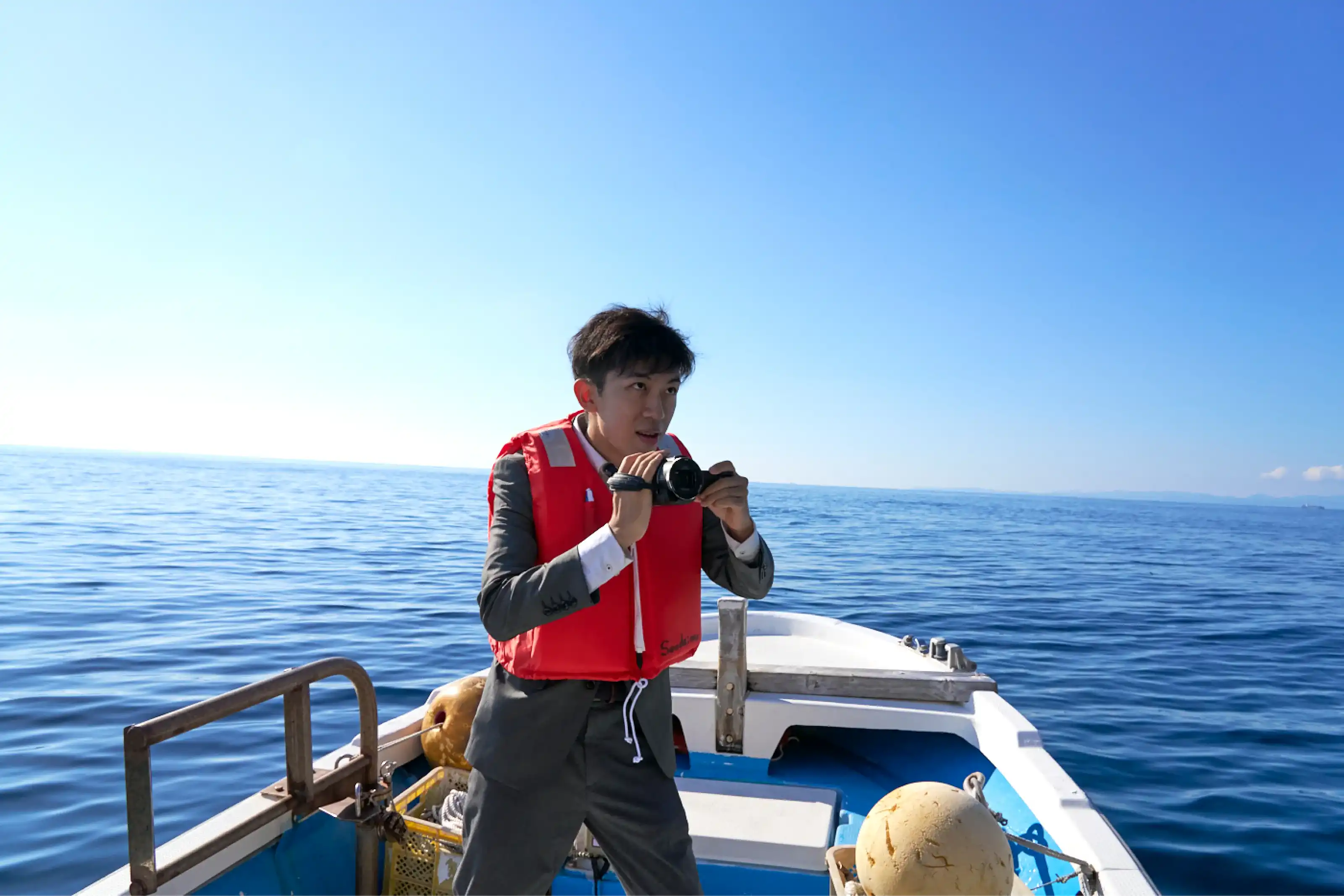 漁船の上でカメラを構えるスーツさん