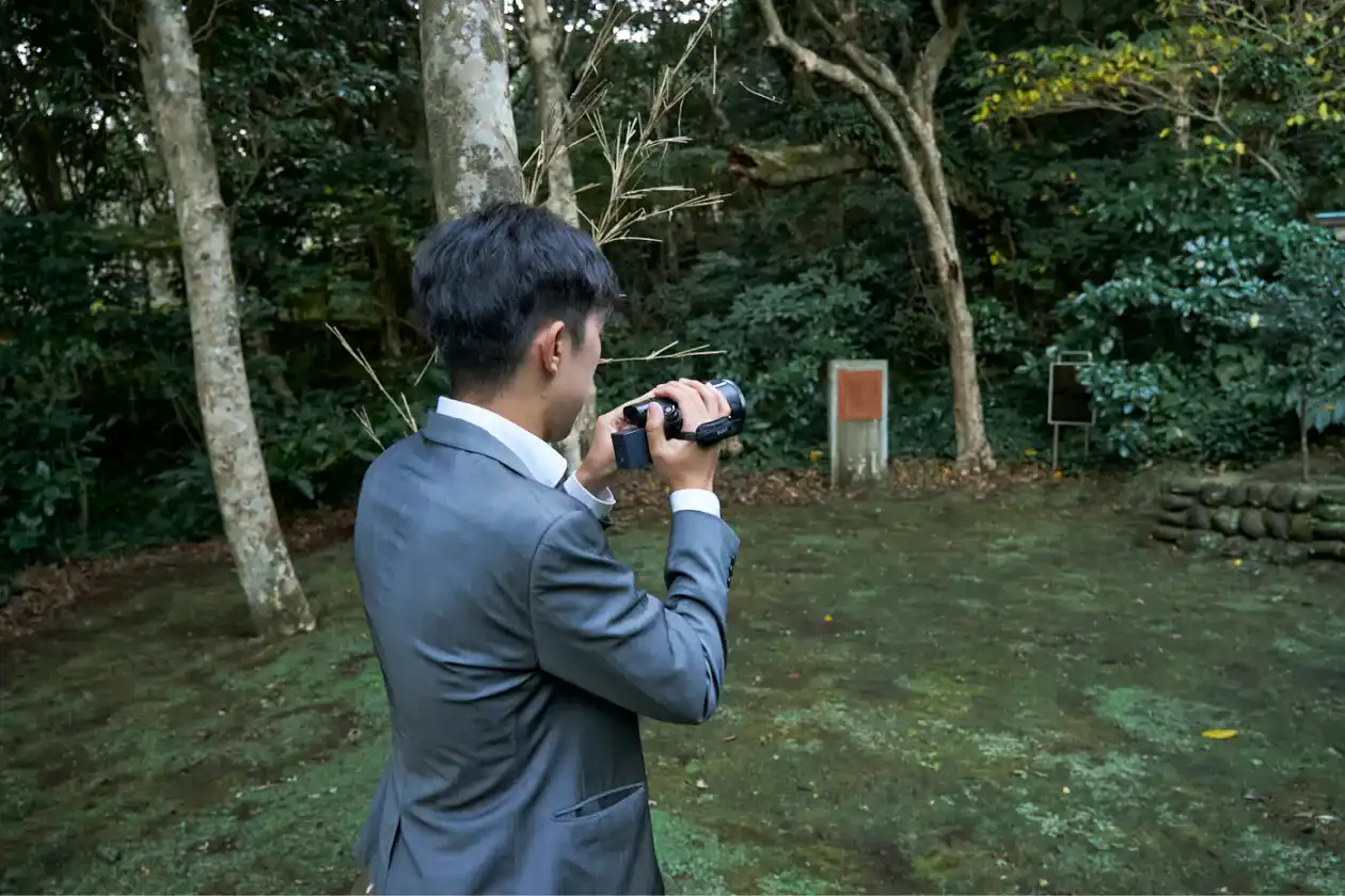 森の中でカメラを構えるスーツさん