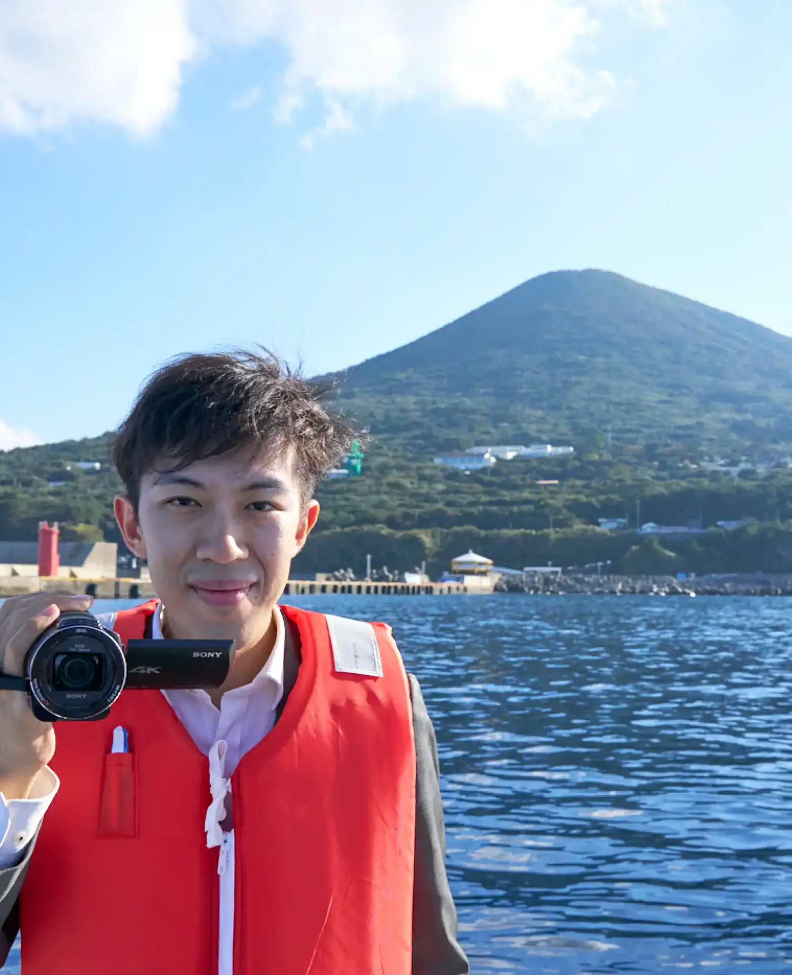 宮塚山をバックにカメラを構えるスーツ旅行さん